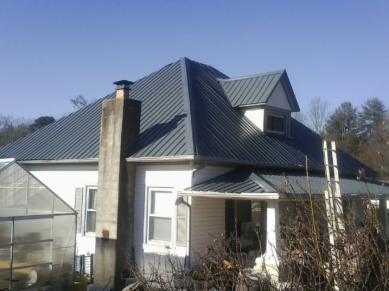 Dark blue standing seam metal roof on a white farmhouse with dormer — Slate & Tile Roof Repair by Roofing Brothers in Eagle Lake
