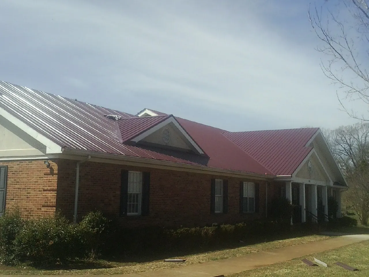 Red metal roof with gabled entries on a long brick building, from a Hail Damage Roof Repair job in Eagle Lake