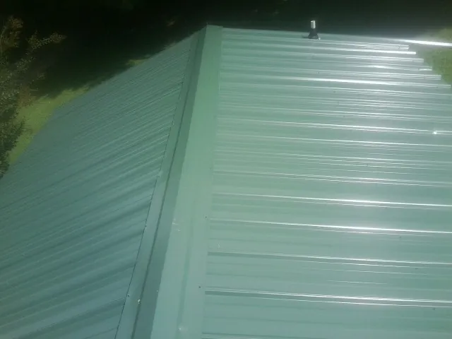 New green metal panels meeting at the ridge of a roof — Flat Roof Repair work by our crew in Eagle Lake