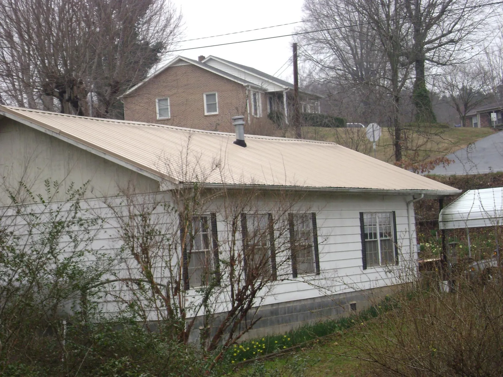 Tan metal roof on a white sided house set into a hillside — Commercial Roofing by Roofing Brothers in Eagle Lake