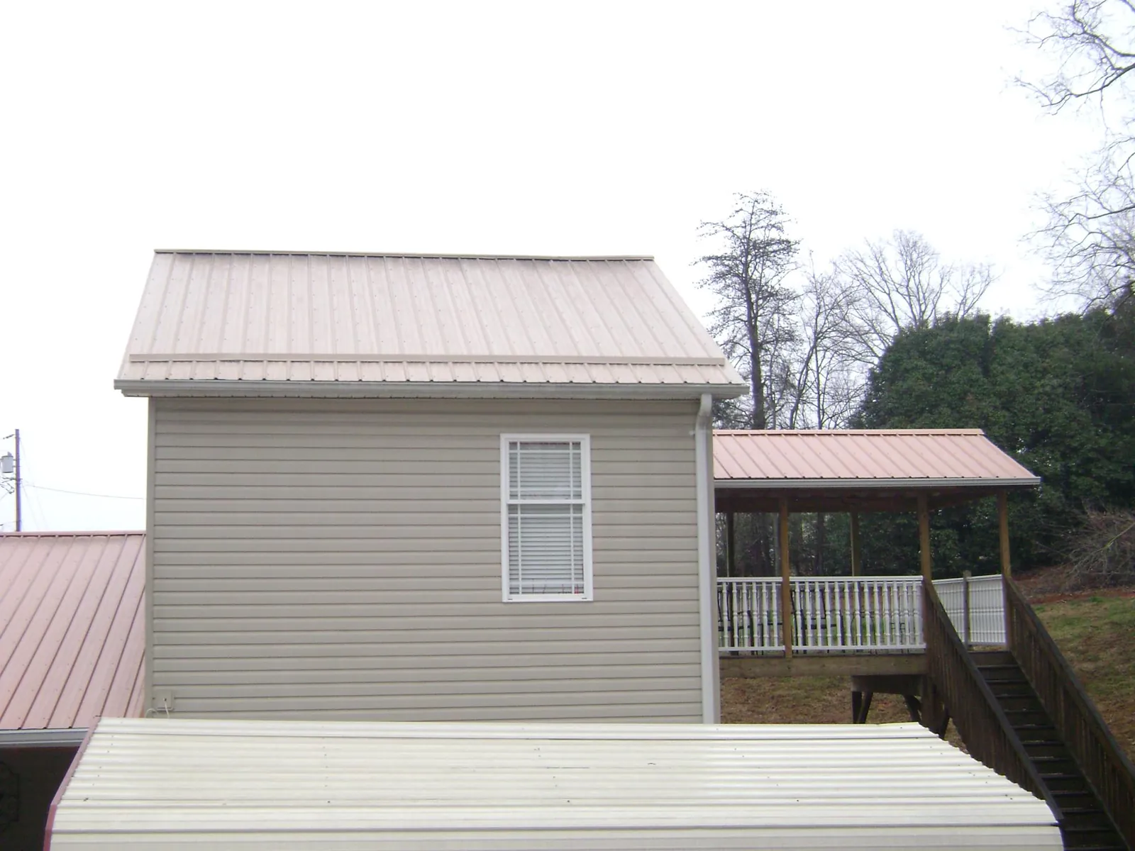Tan metal roofs on a two story addition and attached porch, from a Roof Replacement job in Eagle Lake